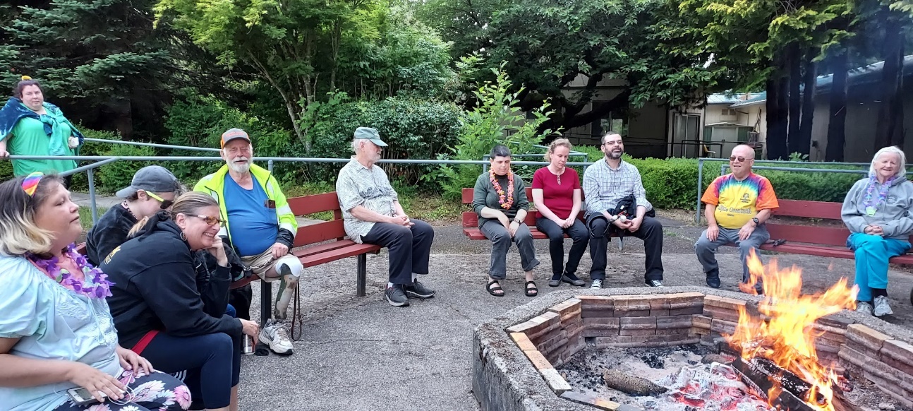 A group of people sitting on benches around a fire pit Description
automatically
generated