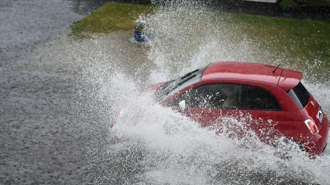 Ein Auto fährt über eine überschwemmte Straße und sorgt für sehr große Wasserspritzer
