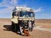 Ein Mann, eine Frau und ein Hund stehen vor einem umgebauten Bundeswehr-Lkw in Merzouga in Marokko.