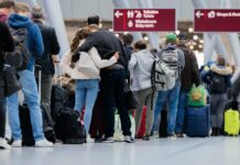 Viele Passagiere stehen an einer Schlange in einem Flughafen und warten.
