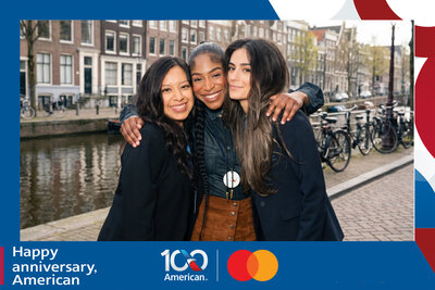 AI travel photo experience for American Airlines' 100th anniversary with Mastercard: three guests embrace along an Amsterdam canal lined with bikes and gabled houses.