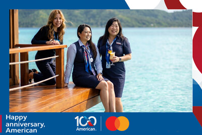 AI travel photo experience for American Airlines' 100th anniversary with Mastercard: three guests relax on an overwater bungalow deck above a turquoise lagoon, cocktail in hand.