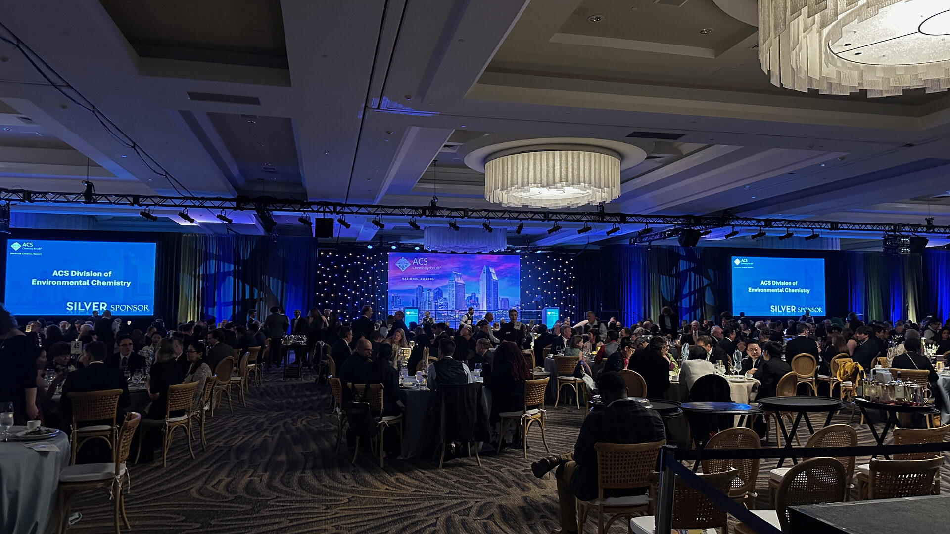 Ballroom full of seated guests during an awards ceremony with stage screens